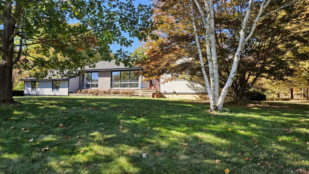 House surrounded by trees and grassy lawn.