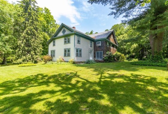Two-story house surrounded by trees, sunny day.