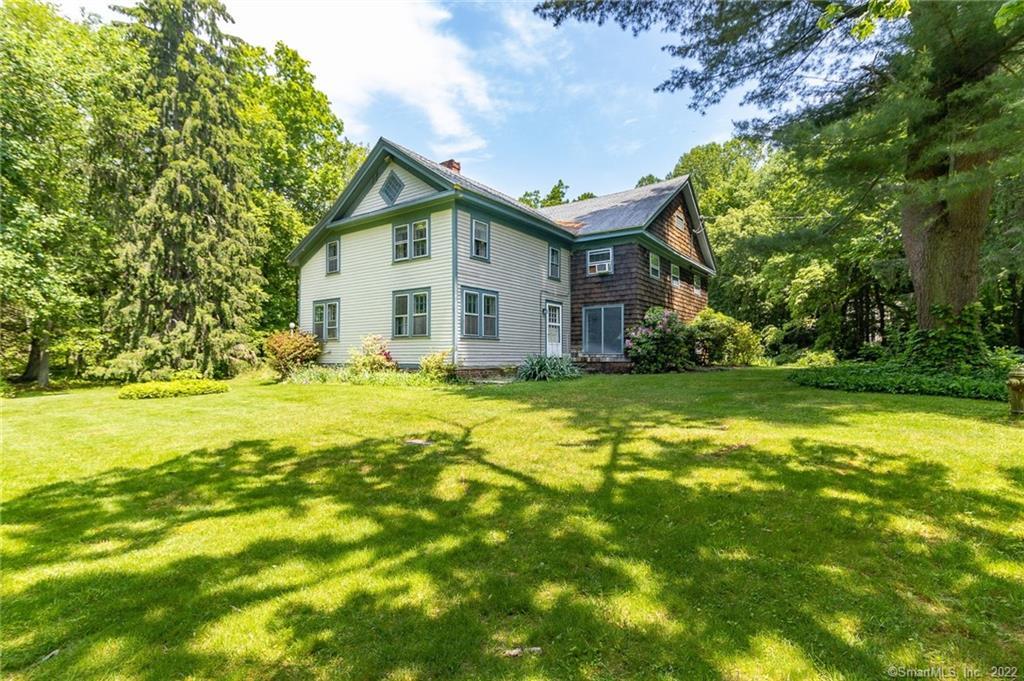 Two-story house surrounded by trees, sunny day.
