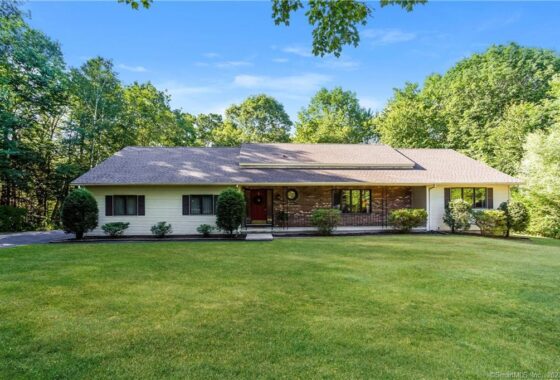 Single-story house with a large green lawn and surrounding trees.