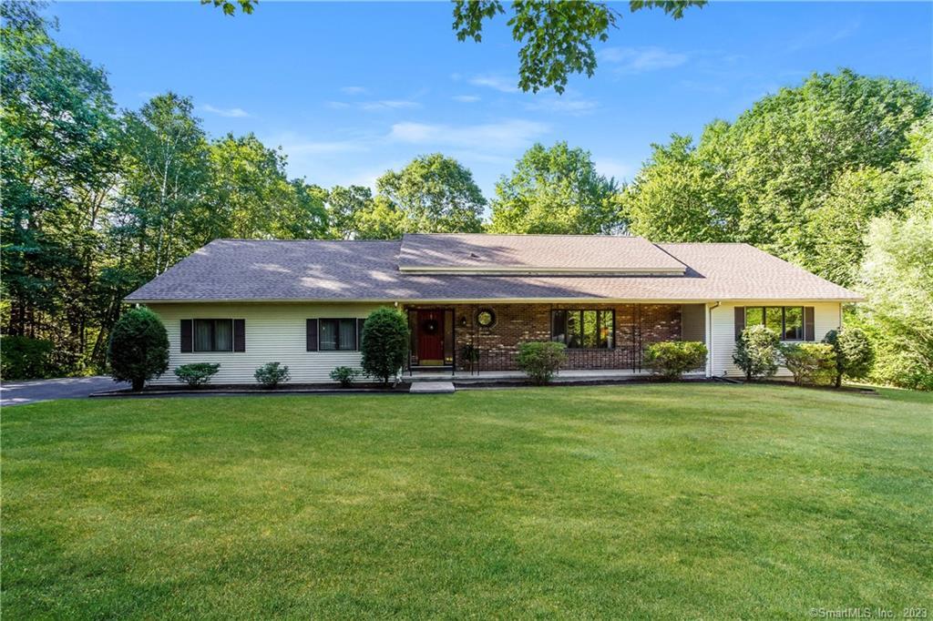 Single-story house with a large green lawn and surrounding trees.