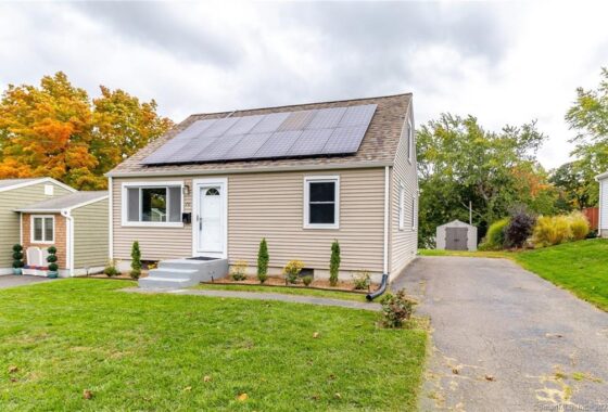 Small beige house with solar panels on the roof and a green lawn.
