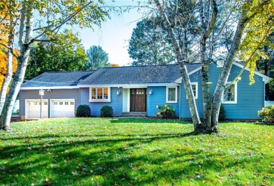 A charming single-story house with a large front yard and mature trees.