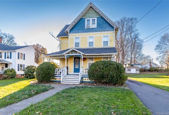 A charming yellow and blue Victorian house with a spacious front yard.
