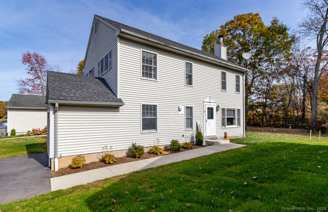 White two-story house with a gray roof and green lawn under a clear sky.