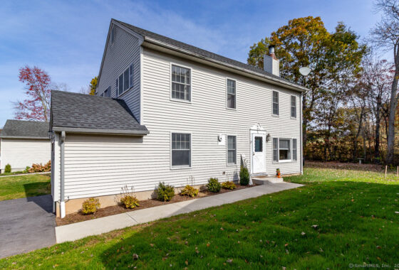 White two-story house with a gray roof and green lawn under a clear sky.