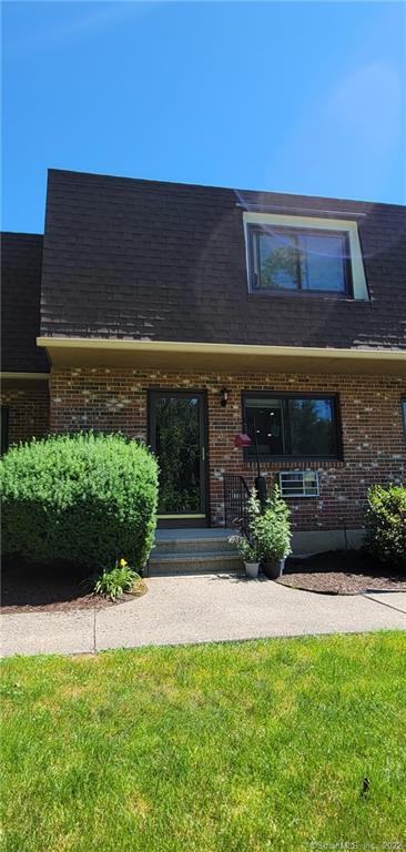 Brick house entrance with green shrub and potted plant on the porch.