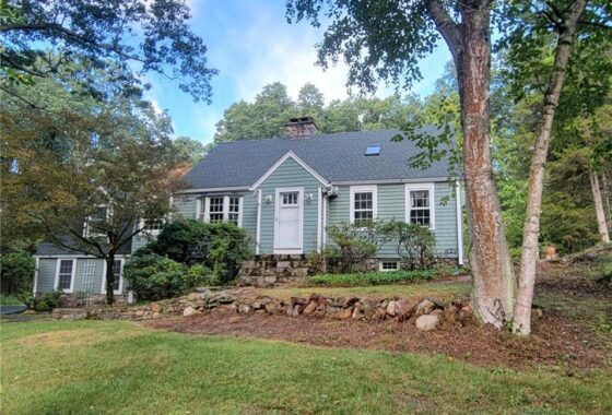 Charming grey house with a stone retaining wall and lush greenery.