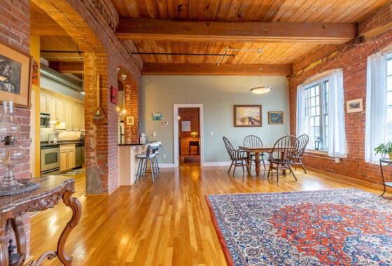 Spacious living room with wooden floors and ceiling, furnished with a dining table and rug.