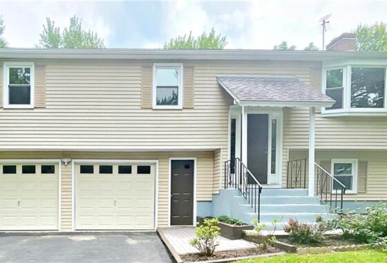 A two-story house with beige siding, a garage, and a small front porch with steps.