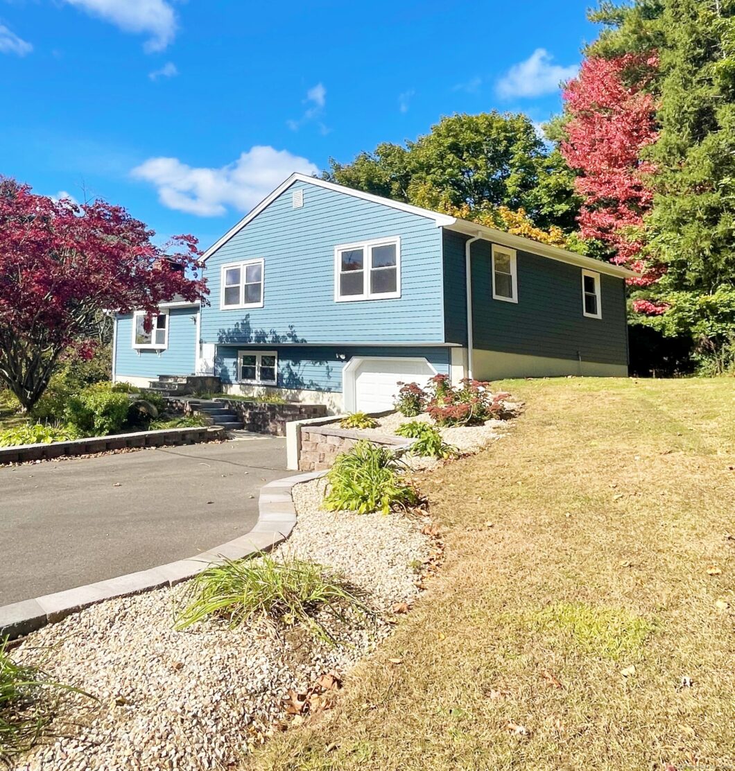 A blue house with a driveway and colorful autumn trees.