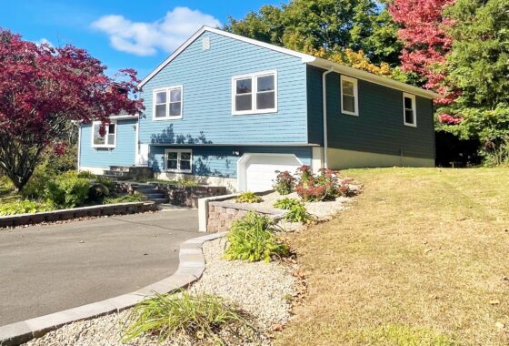 A blue house with a driveway and colorful autumn trees.